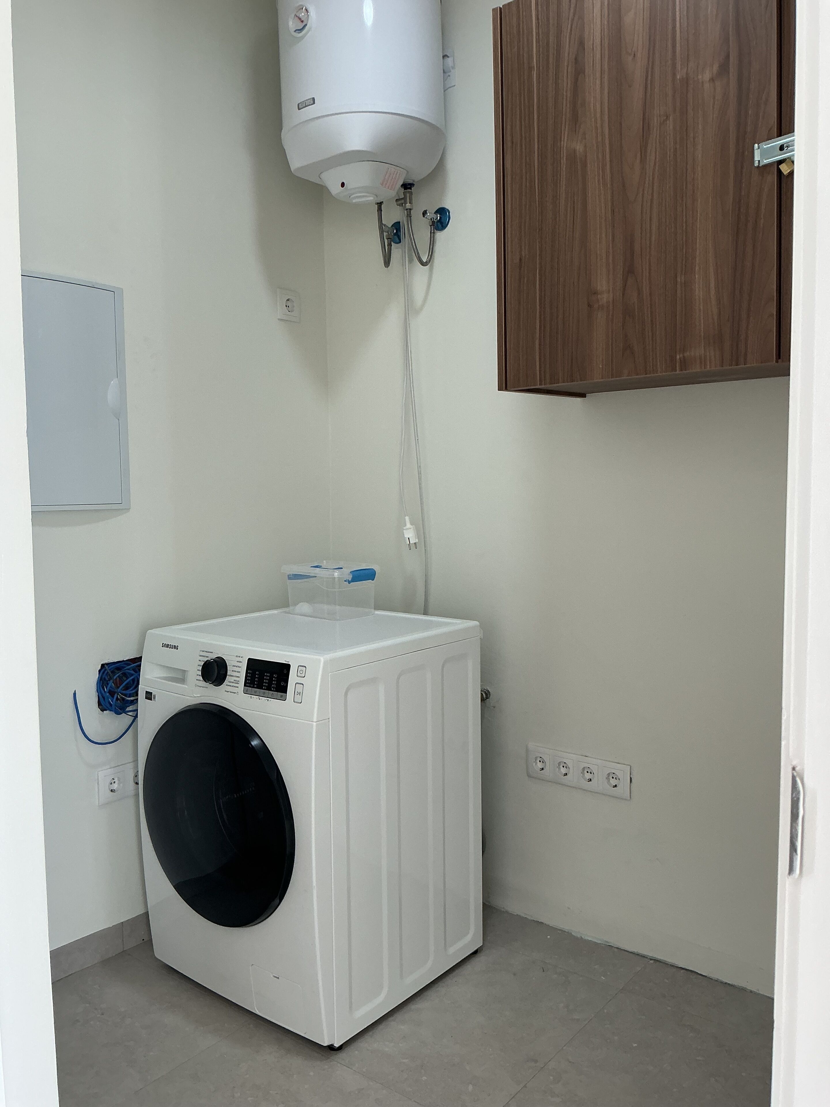 A laundry room with a white washing machine, a water heater, and a wooden cabinet.