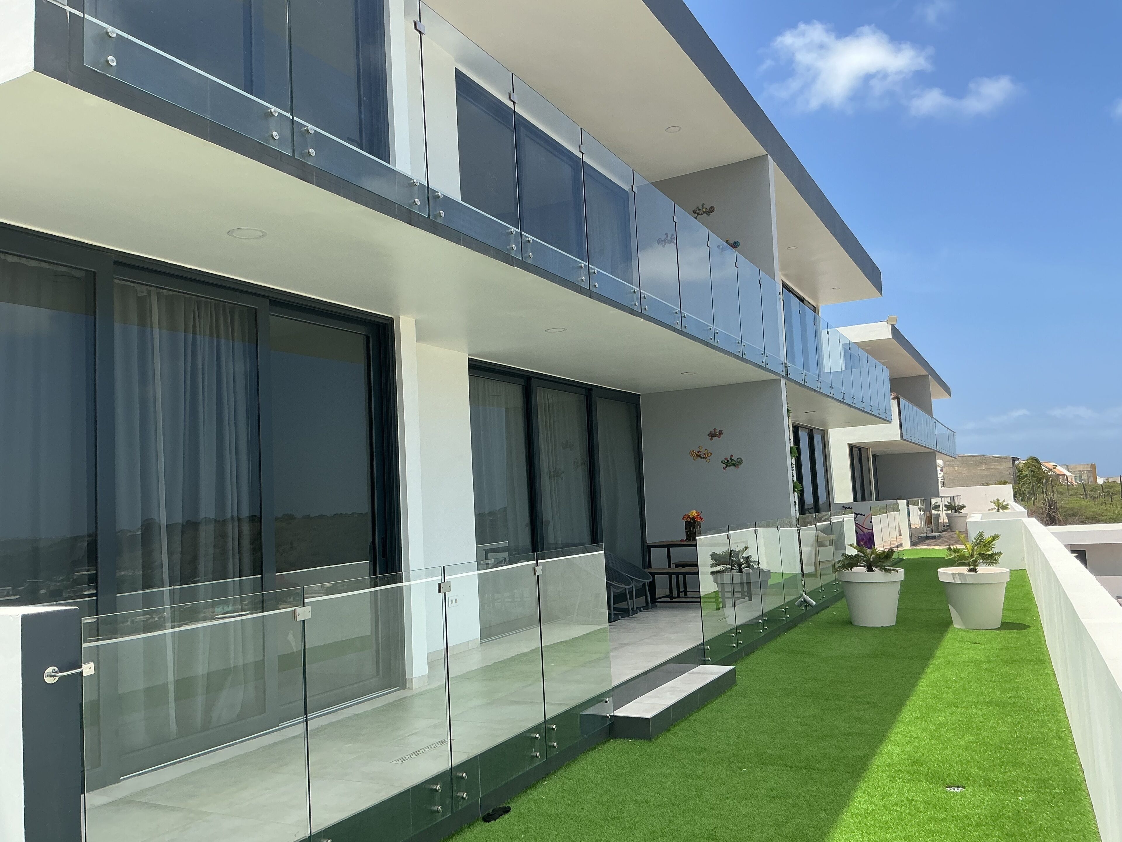 Un immeuble résidentiel moderne à deux étages, doté de grandes fenêtres en verre, d’un balcon et d’une pelouse bien entretenue.