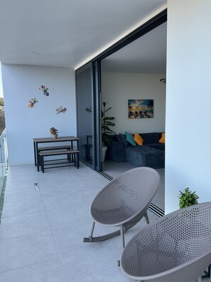 Een moderne woonruimte met een schuifdeur naar een balkon, een bank met kleurrijke kussens, een eettafel met stoelen, en decoratieve wanddecoratie.