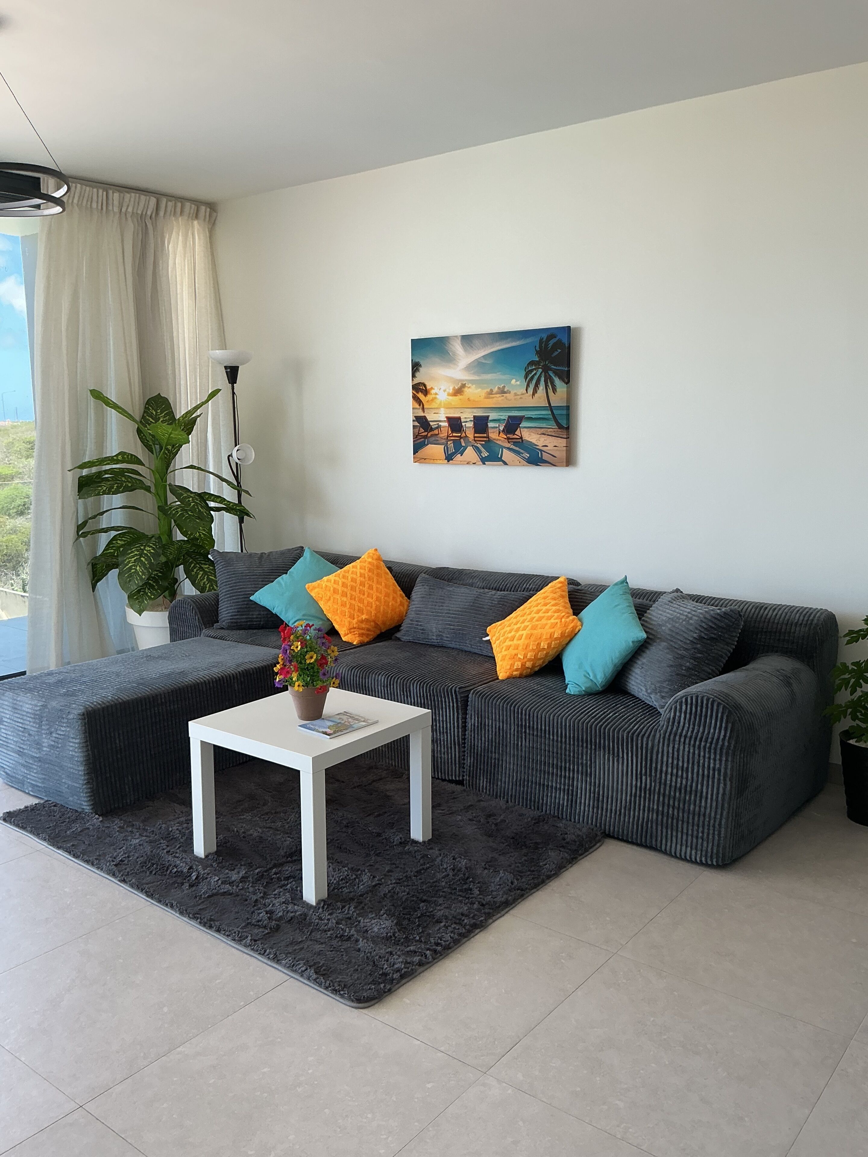 Una sala de estar con un sofá modular, una mesa de centro y un cuadro con una escena de playa.