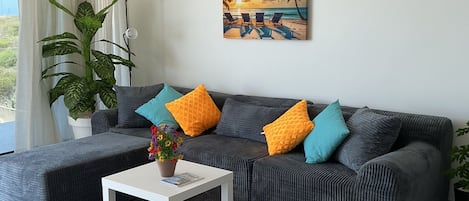 Una sala de estar con un sofá modular, una mesa de centro y un cuadro con una escena de playa.