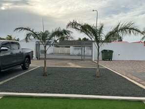 Een parkeerplaats met een grindoppervlak, een groene rand van kunstgras en een hekwerk.