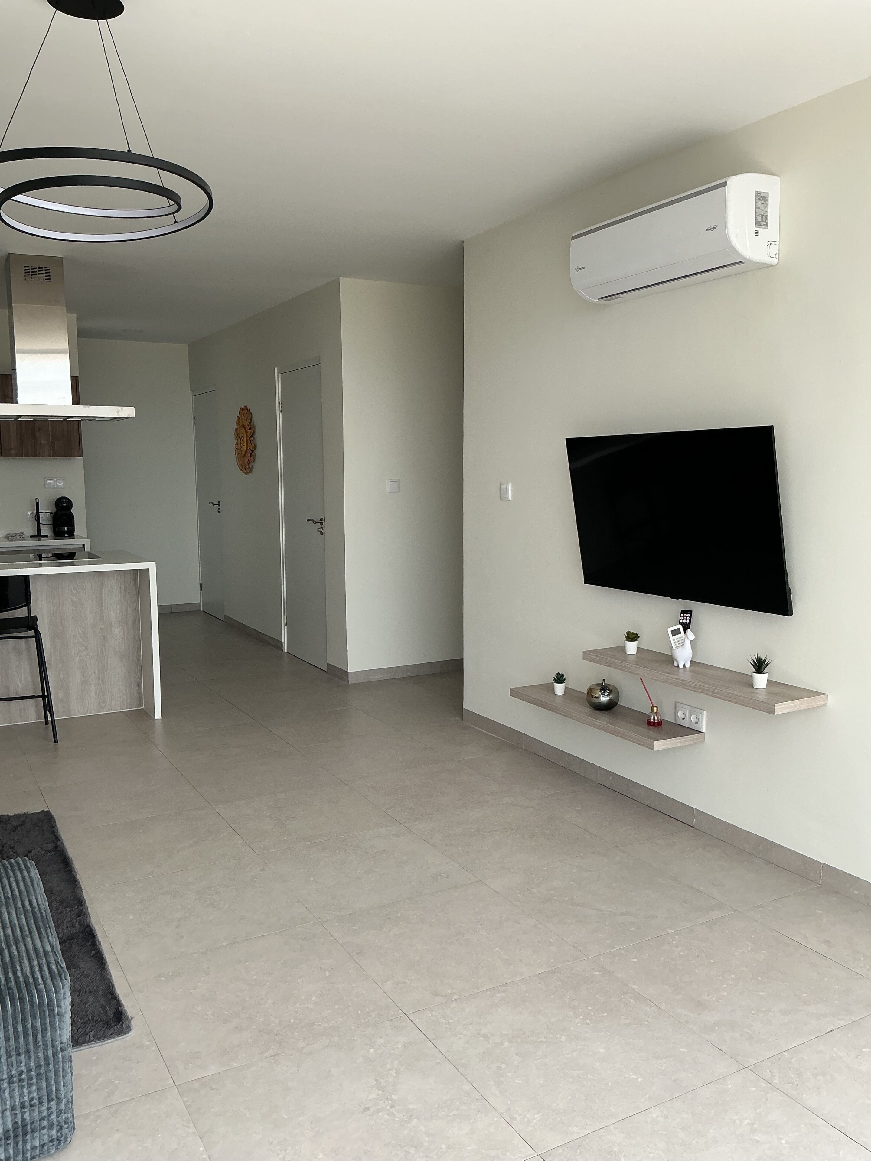 A modern living room with a flat-screen TV mounted on a wooden shelf, a ceiling fan, and a built-in air conditioning unit.
