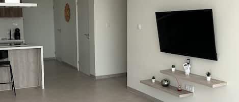 Un salon moderne doté d’un téléviseur à écran plat fixé sur une étagère en bois, d’un ventilateur de plafond et d’un système de climatisation intégré.
