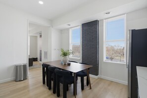 A modern dining area with a wooden table and chairs, a potted plant, and a black brick accent wall.
