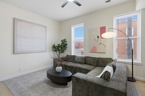 A living room with a sectional sofa, a round coffee table, a floor lamp, and artwork on the walls. - Beautiful 3-bedroom apartment with AC in charming St. Louis (St. Louis)