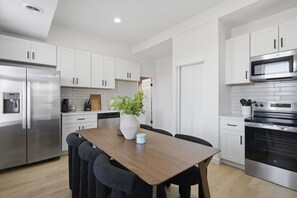 A modern kitchen with white cabinets, stainless steel appliances, and a wooden dining table. - Beautiful 3-bedroom apartment with AC in charming St. Louis (St. Louis)