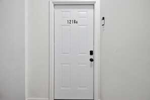 A white door with the number 1216A, a keyhole, and a doorbell on the right side.