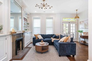 A living room with a fireplace, a blue sofa set, a round coffee table, and a chandelier. - Charming Historic Row Home in Lincoln Park (Chicago)