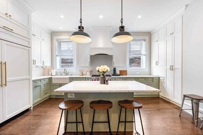 A spacious kitchen with a large island, pendant lighting, and a view of the city through the windows. - Charming Historic Row Home in Lincoln Park (Chicago)