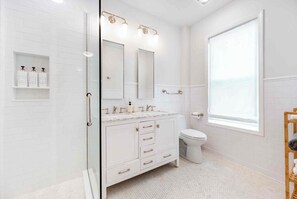 Une salle de bain moderne avec un meuble-lavabo blanc, une cabine de douche en verre et une grande fenêtre.