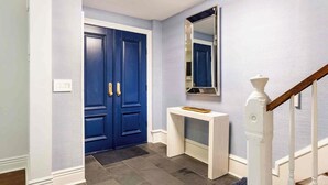 Un pasillo con una puerta azul, un mueble consola blanco y un espejo en la pared.