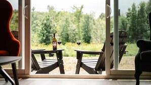 A view through a glass door with a table and chairs outside, a bottle of wine, and two glasses on the table. - New Vineyard Cottage in Niagara Wine Country | 2BR (Lincoln)