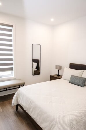 Ein Schlafzimmer mit Bett, Nachttisch, Lampe und einem Fenster mit Jalousien.