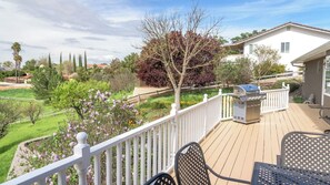 Eine Terrasse mit Gartenmöbeln und Grill, umgeben von einem weißen Zaun und einem Garten mit blühenden Pflanzen.