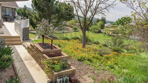 Ein Wohnhaus mit Terrasse, Sitzgelegenheiten im Freien, einer Feuerstelle und einem Garten mit Blumen.