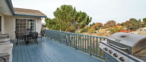 A deck with outdoor furniture, a grill, and a view of trees and houses.