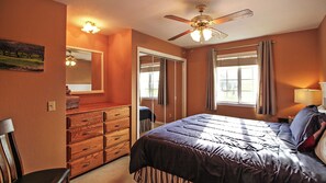 Une chambre à coucher avec un lit, une commode, un ventilateur de plafond et une fenêtre.