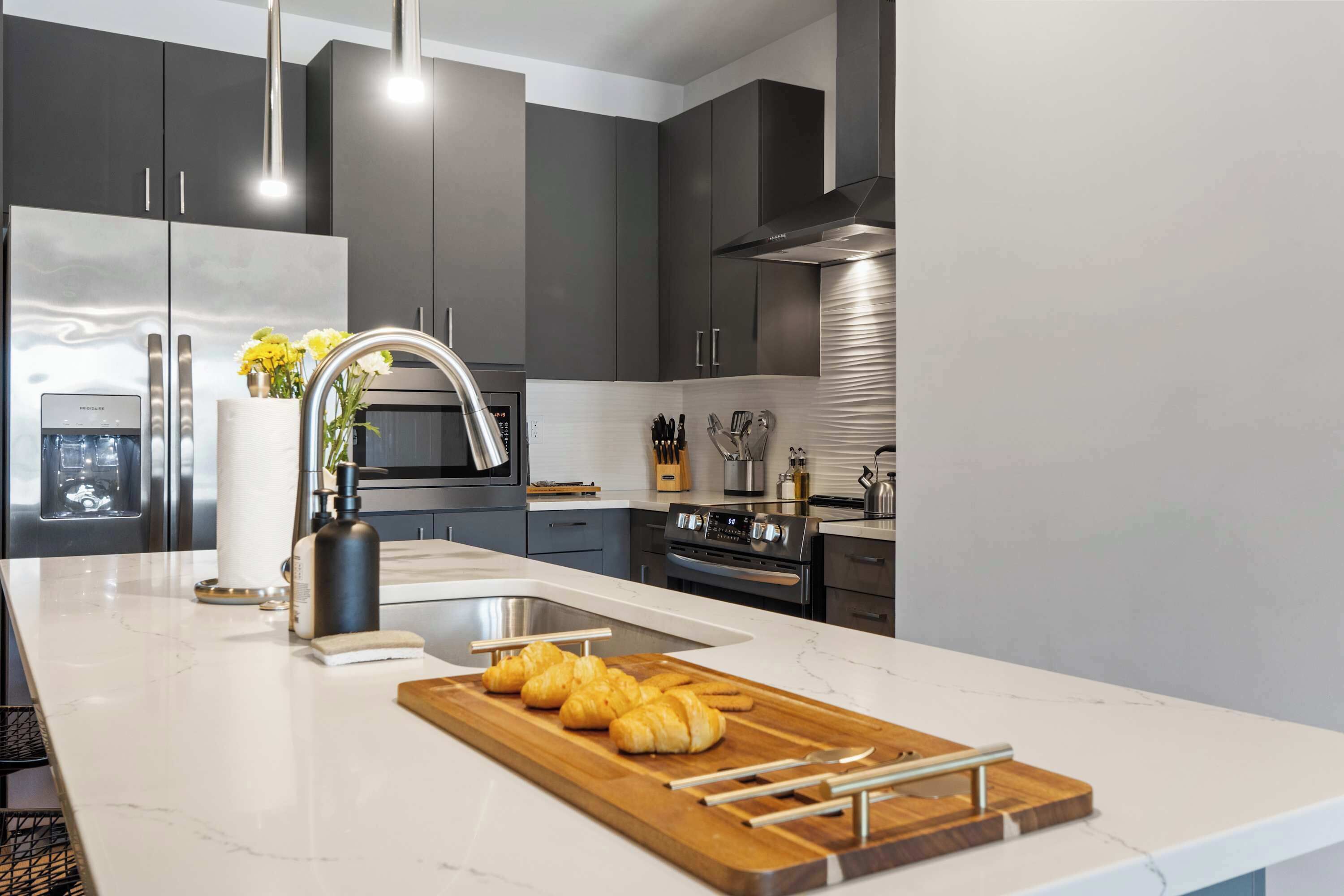 A modern kitchen with dark cabinets, stainless steel appliances, and a marble countertop.