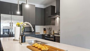 A modern kitchen with dark cabinets, stainless steel appliances, and a marble countertop. - Urban & Soulful Escape: 2 Condos Near Vandy | Pool (Nashville)