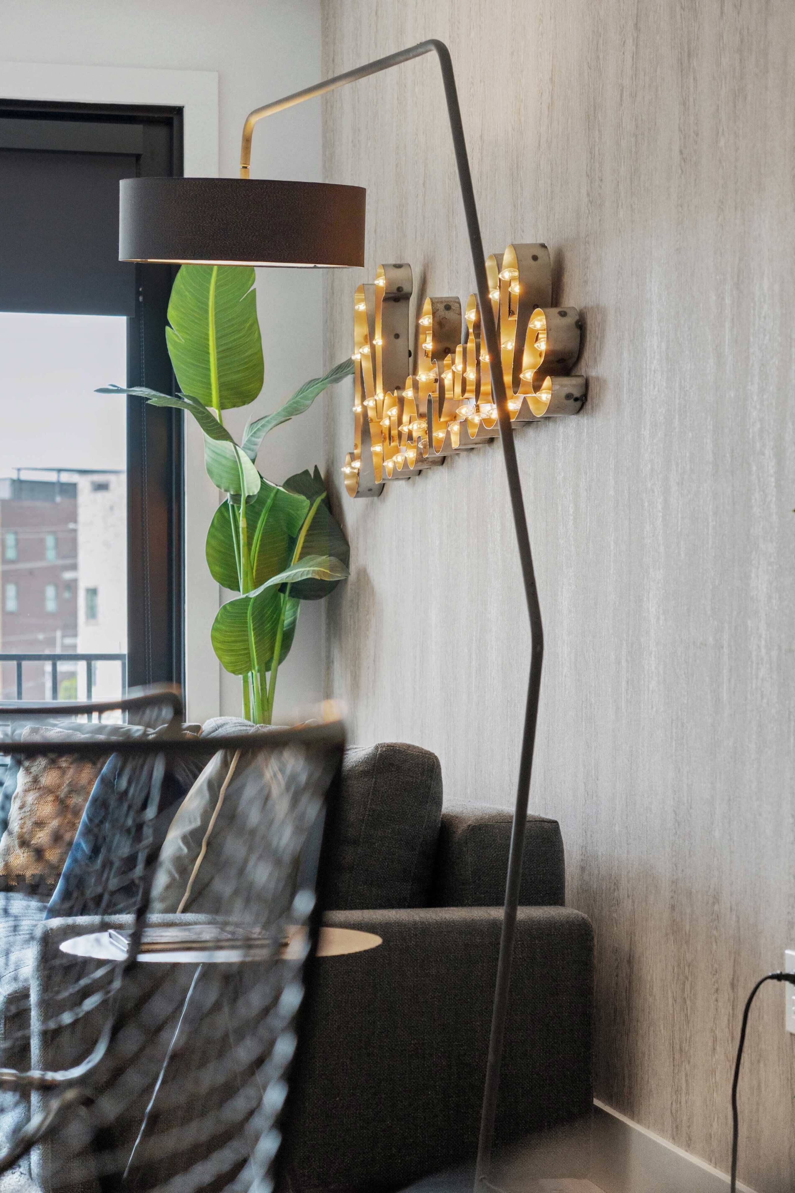A modern living room with a sofa, a floor lamp, a wall-mounted light fixture, and a potted plant.