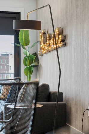 A modern living room with a sofa, a floor lamp, a wall-mounted light fixture, and a potted plant. - Urban & Soulful Escape: 2 Condos Near Vandy | Pool (Nashville)
