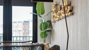 A modern living room with a sofa, a coffee table, a floor lamp, and a wall-mounted light fixture. - Urban & Soulful Escape: 2 Condos Near Vandy | Pool (Nashville)