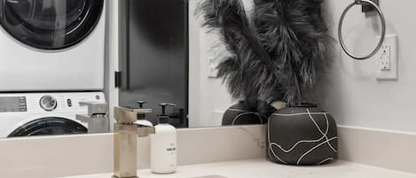 Un baño moderno con un lavamanos blanco, un espejo, una lavadora y un perchero para toallas.