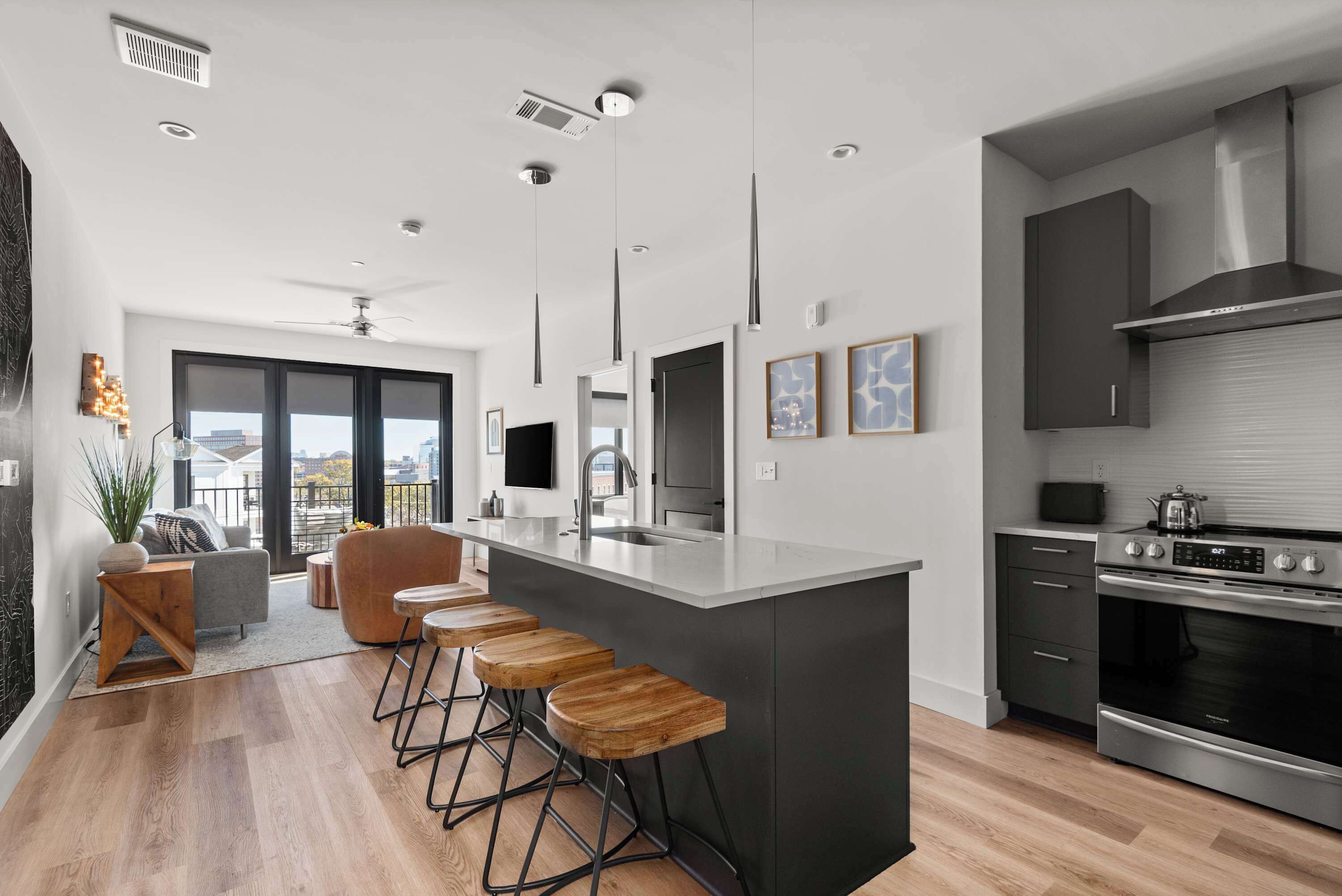 A modern kitchen with a central island, bar stools, and a view to the outside.