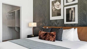 A hotel room with a bed, a nightstand, a lamp, a closet, and a wall with framed pictures. - Urban & Soulful Escape: 2 Condos Near Vandy | Pool (Nashville)