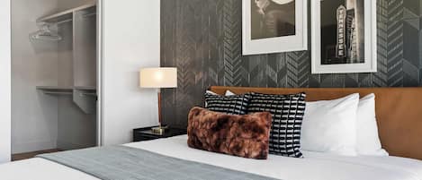 A hotel room with a bed, a nightstand, a lamp, a closet, and a wall with framed pictures.
