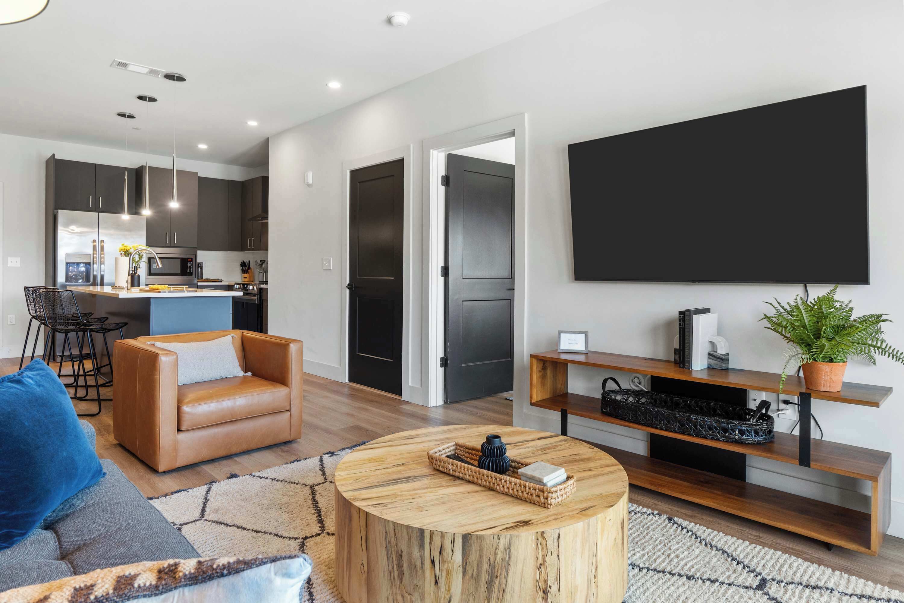 Un salon moderne avec un canapé en cuir, une table basse ronde et un téléviseur à écran plat fixé au mur.