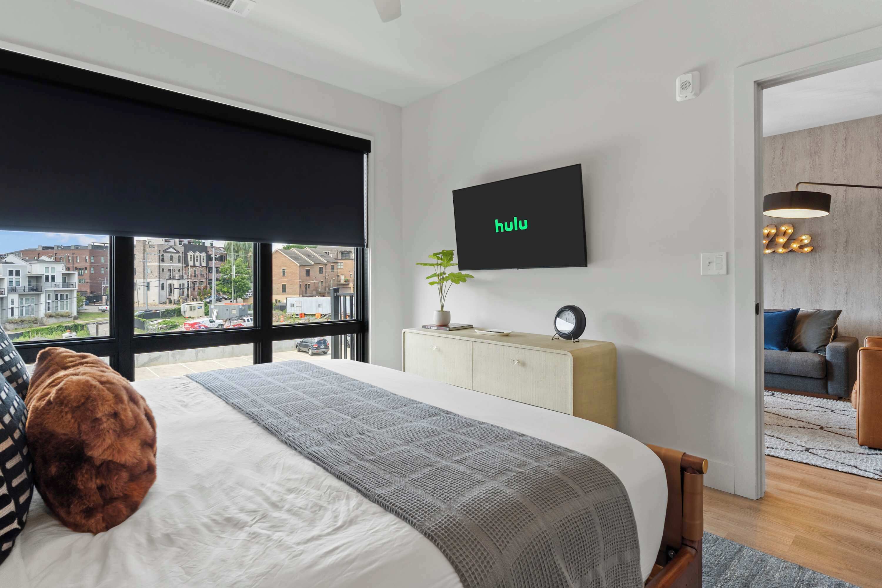 A modern bedroom with a large bed, a TV mounted on the wall, and a view of the city through the window.