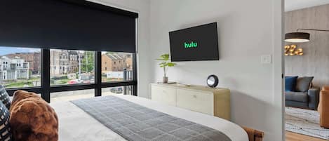 Un dormitorio moderno con una cama grande, un televisor montado en la pared y vistas de la ciudad a través de la ventana.