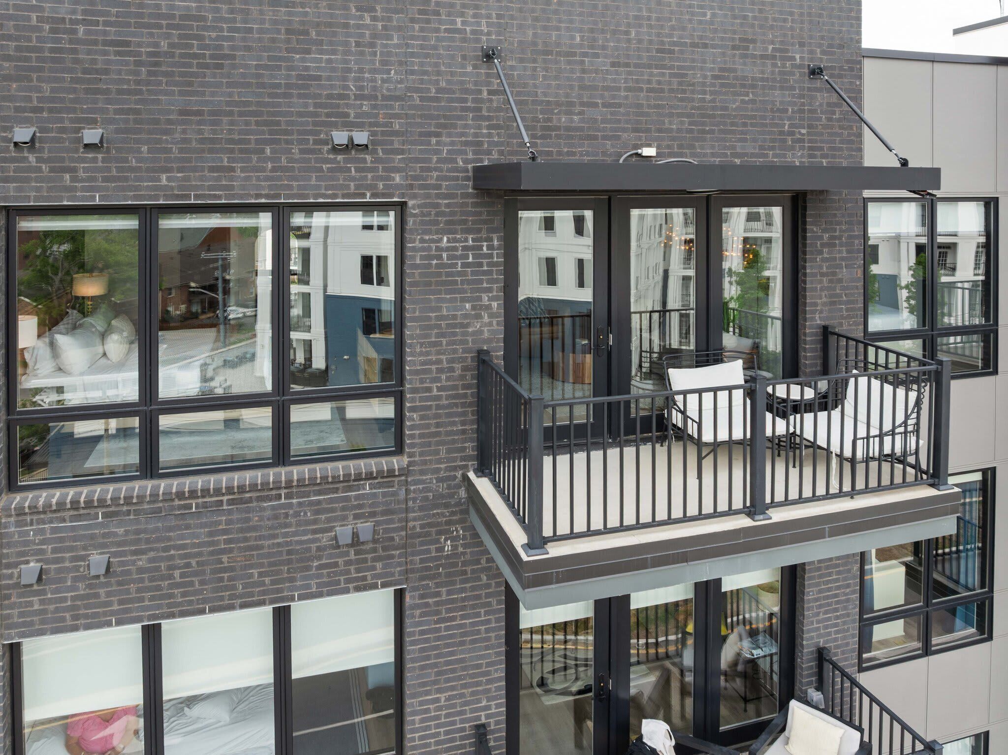 Un edificio de varios pisos con amplias ventanas, un balcón con mobiliario exterior y vistas a la calle.
