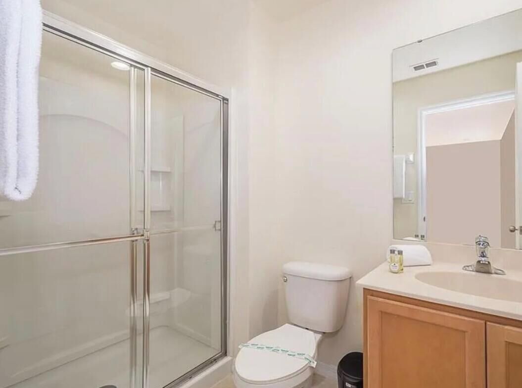 Ein Badezimmer mit Duschkabine aus Glas, Toilette, Waschbecken mit Spiegel und Holzschränken.