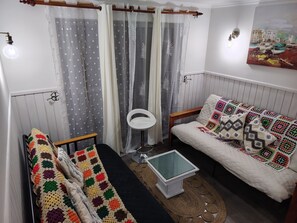 A cozy room with a bed, a small table, and a chair. There is a window with curtains, a wall-mounted light fixture, and a painting. - A warm and cozy apartment located in a peaceful, natural, and relaxed setting (Araucanía)