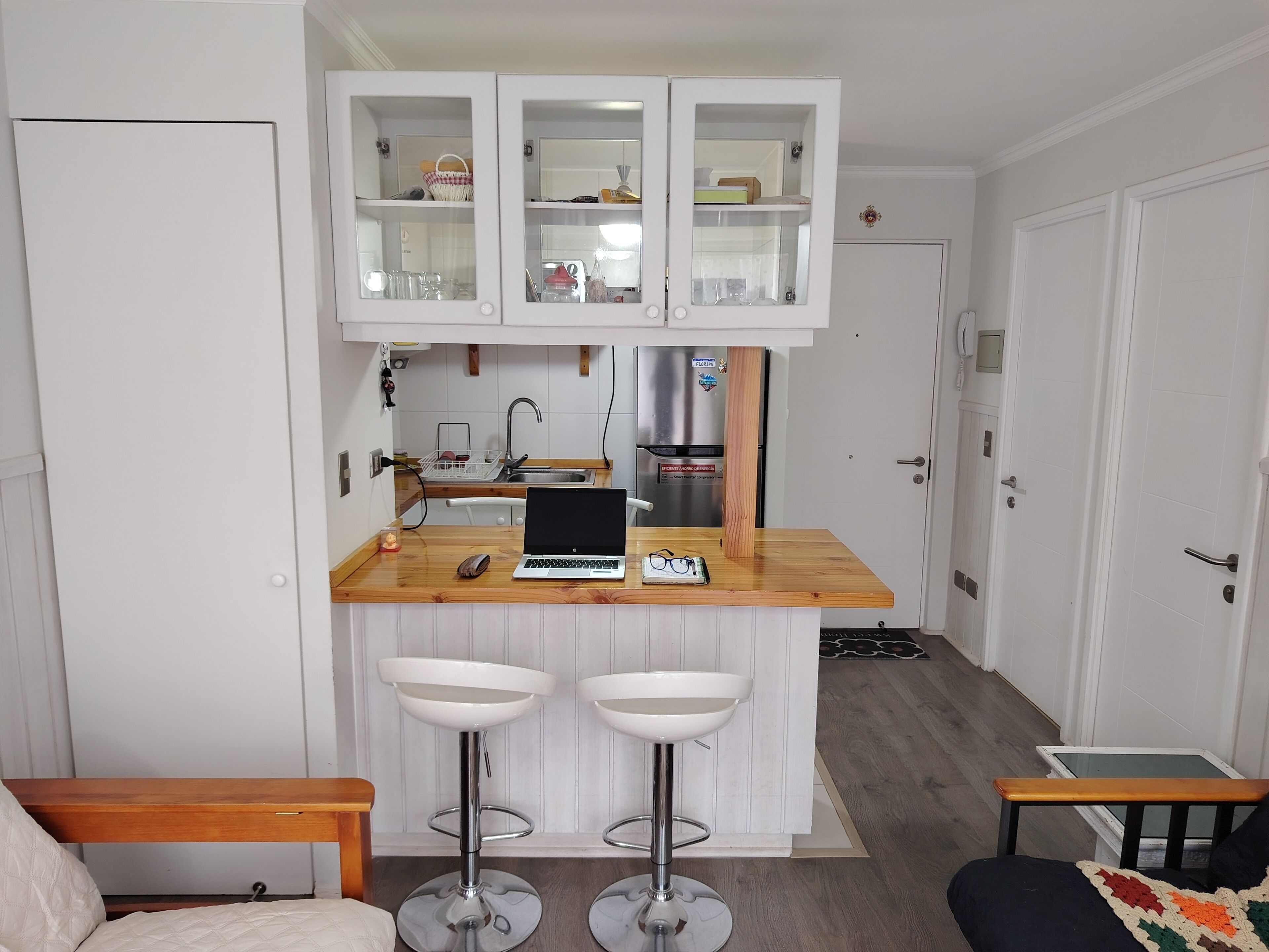 A compact kitchen with a built-in island, two bar stools, and a laptop on the counter.