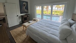 Quarto com cama grande, ventoinha no teto, vista para uma piscina e porta que dá para outro cômodo.