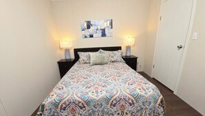 A bedroom with a patterned bedspread, two bedside lamps, a wall art piece, and a door. - Charming 2bedroom house in Mission , a few minutes to Shary Rd and La Plaza Mall (Mission)