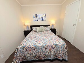 Un dormitorio con una colcha estampada, dos lámparas de noche, una obra de arte en la pared y una puerta.