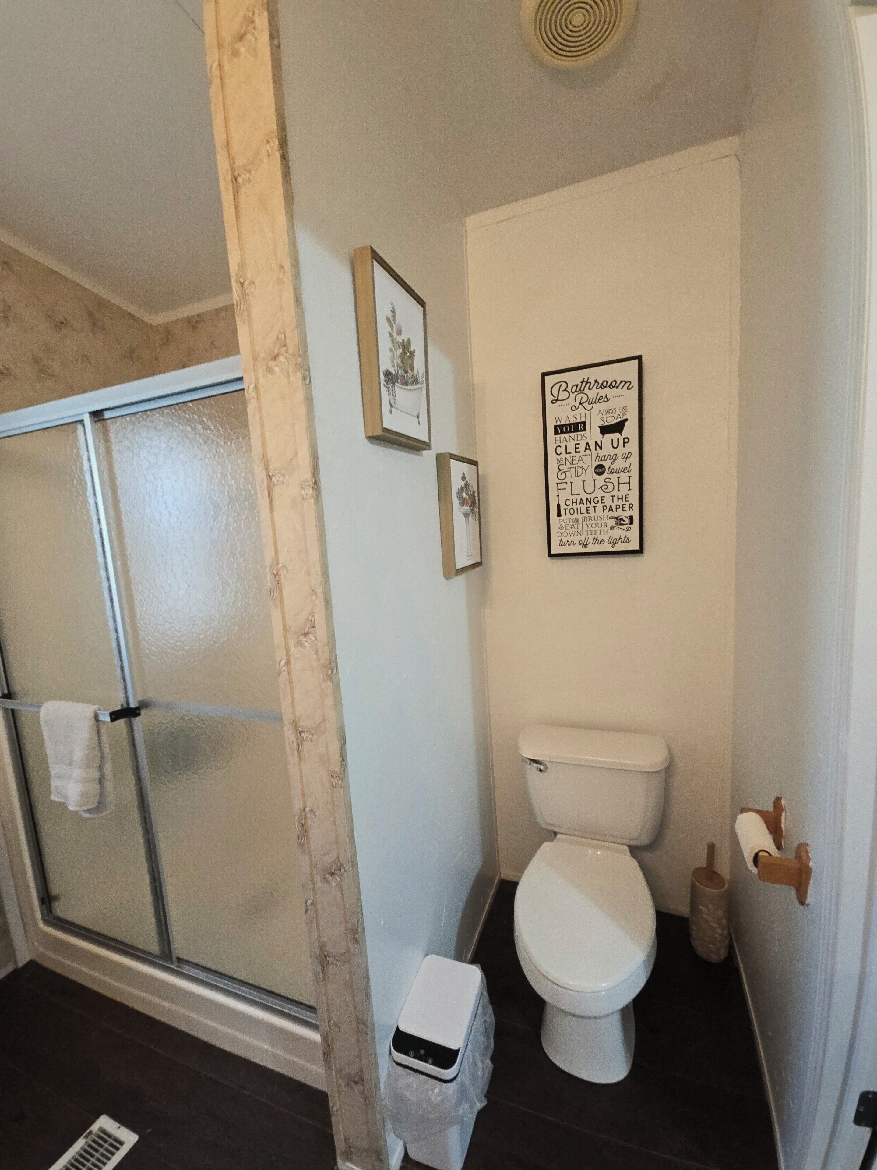 Une salle de bain équipée de toilettes, d’une douche et d’un panneau affichant les règles d’utilisation, fixé au mur.