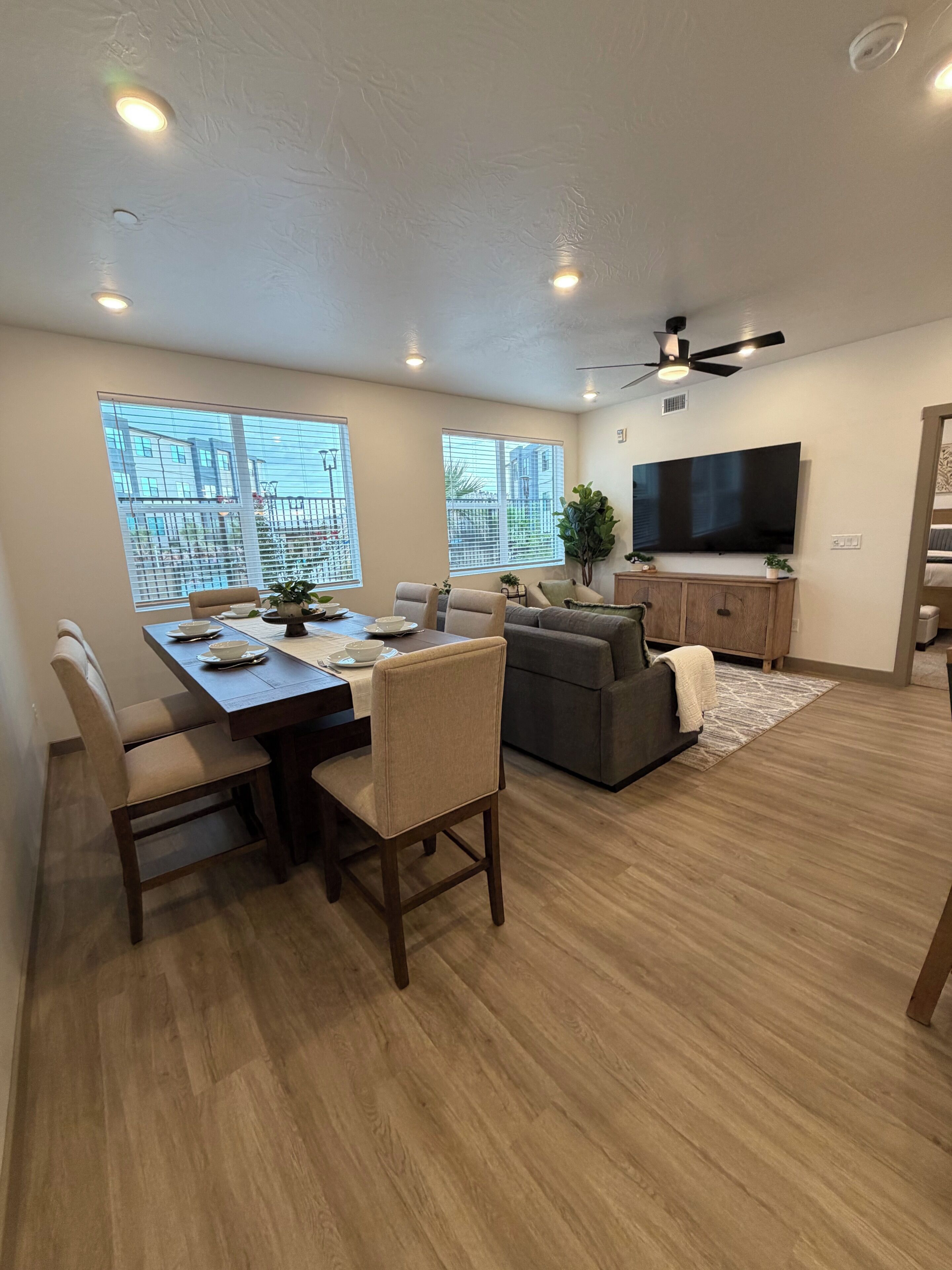 Una sala de estar moderna con comedor, ventanas amplias, televisor de pantalla plana y ventilador de techo.