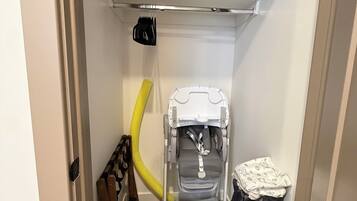 A storage closet with shelves, a stroller, a vacuum cleaner, and a trash bag.