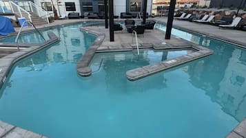 A swimming pool with a pergola, lounge chairs, and a view of apartment buildings.