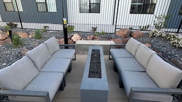 An outdoor seating area with two sofas and a central table, surrounded by a metal fence and a building with windows.