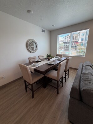 A dining area with a wooden table, beige chairs, and a wall clock. - TLC Retreat (Hurricane)