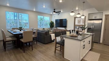 A spacious living area with a dining table, sofas, and a kitchen with a refrigerator.