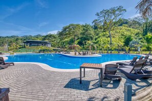 A swimming pool with lounge chairs and a table, surrounded by greenery and a building in the background. - Casa Esmeralda Luxury Retreat (Jacó)