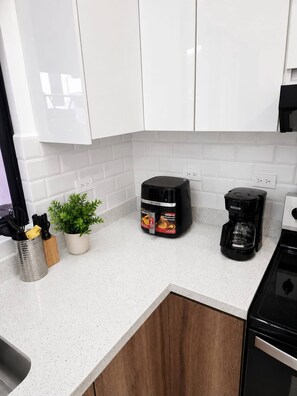 A kitchen with white cabinets, a coffee maker, a container of coffee pods, a potted plant, and a utensil holder. - Casa Esmeralda Luxury Retreat (Jacó)